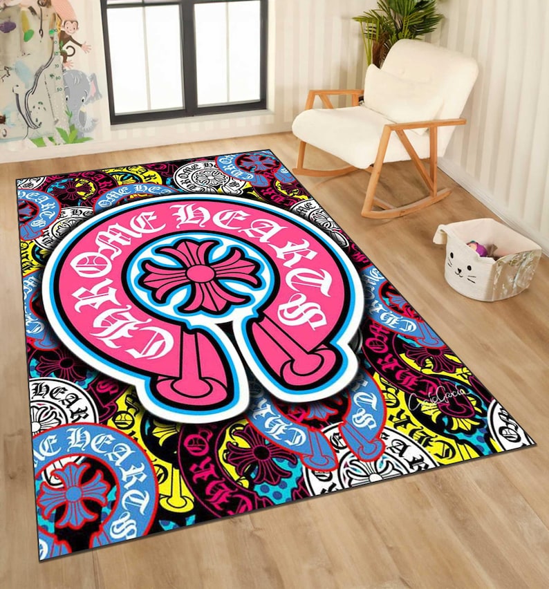 May include: A rectangular area rug with a vibrant, multi-colored design. The rug features a large, pink and white emblem with the words "Chrome Hearts" and a cross-shaped design. The background is filled with various patterns and colors, including blue, yellow, and black.