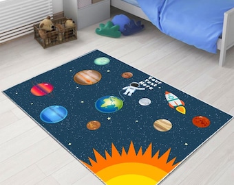 May include: A rectangular rug with a space theme. The rug features planets, stars, an astronaut, and a rocket ship against a dark blue background. The bottom of the rug has a large orange and yellow sun. Text on the rug reads "Your text here."