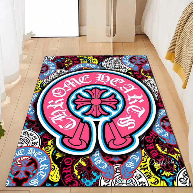 May include: A rectangular rug with a vibrant, multi-colored design. The central focus is a large, pink emblem with the words "CHROME HEARTS" in white, surrounded by a blue outline. The rug features a repeating pattern of circular emblems in various colors.