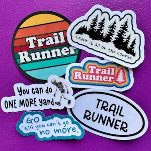 Könnte beinhalten: Eine Sammlung von sechs Vinyl-Aufklebern mit Trailrunning-Motiven. Die Designs umfassen einen Sonnenuntergangskreis mit 'Trail Runner', eine Waldsilhouette mit 'Leave it all on the course', ein Skelett mit 'You can do ONE MORE yard' und 'GO 'till you can't go no more'.