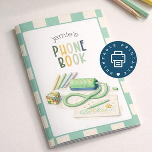 Puede incluir: Un cuaderno con espiral con un borde a rayas verde menta y blanco. La portada dice "PHONE BOOK de Jamie" en letras coloridas. Un círculo azul con un icono de impresora y la palabra "PRINTABLE" está a la derecha. También se ven lápices y un cubo de Rubik.