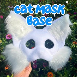 May include: A white cat mask base featuring two large pointed ears and fluffy white faux fur accents on the sides. The mask has two circular eye openings and is constructed from a smooth, solid white material. The text cat mask Base is visible.