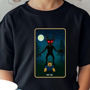 May include: Black t-shirt featuring a graphic of a creature with antlers and glowing red eyes, standing over a block figure, set against a forest and moon backdrop. The word "BLACK" is printed at the bottom.
