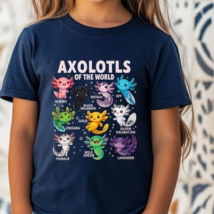 Könnte beinhalten: Marineblaues T-Shirt mit einem farbenfrohen Aufdruck verschiedener Axolotl-Arten, darunter Albino, Black Melanoid und Mosaic. Der Text "AXOLOTLS OF THE WORLD" ist über den Illustrationen abgebildet. Ein Kind trägt das Shirt.