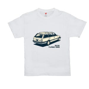 May include: White t-shirt with a cream-coloured station wagon illustration with black and blue accents. The car graphic includes the text "505 TURBO SW8" in a dark blue font. The shirt is made of a soft material.