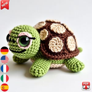 May include: A handmade crochet turtle in shades of green, brown, and beige. The turtle has large, expressive eyes and a detailed shell pattern. The image includes a "NEW" tag and a PDF icon.