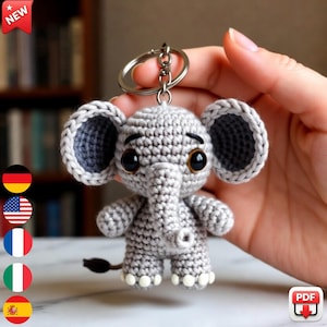 May include: A crocheted gray elephant keychain with large, dark eyes and a small black tail. The elephant has large, floppy ears and white accents on its feet. A silver keyring is attached to the top. The word "NEW" is in a red starburst.