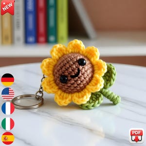 May include: A handmade crochet sunflower keychain with a smiling face. The sunflower has yellow petals, a brown center, and green leaves. The keychain is attached to a silver metal ring. The word "NEW" is in a red banner in the top left corner.