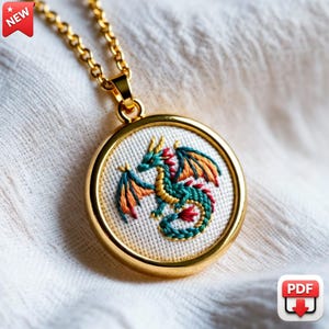 May include: Gold-toned pendant necklace featuring an embroidered dragon design. The dragon is rendered in shades of green, orange, yellow, and red, set against a white background. The pendant is round and has a gold-colored chain. The image has a "NEW" tag.