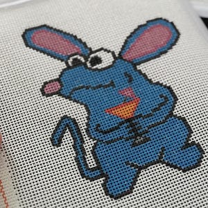 May include: Close-up of a cross-stitch project featuring a blue cartoon mouse with pink ears and a pink nose. The mouse is smiling and has an orange mouth. The project is on white canvas with a plastic frame.