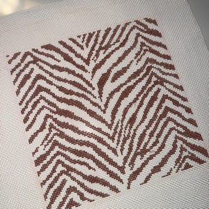 May include: A square needlepoint canvas featuring a brown zebra stripe pattern on a white background. The canvas is made of a mesh material, and the zebra stripes are evenly spaced and detailed.