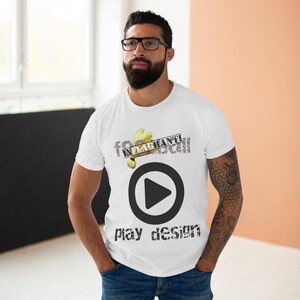 Pode incluir: Camiseta branca com um gráfico de botão de reprodução preto e as palavras "play design" em uma fonte desgastada. A camiseta também apresenta o texto "fo INLAGHANTI call" em uma fonte desgastada. A pessoa está usando jeans azul.