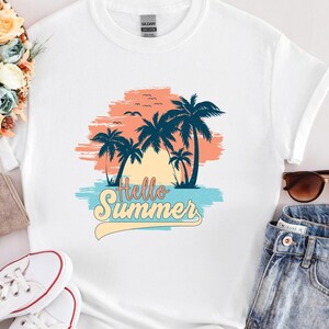 K&ouml;nnte beinhalten: Wei&szlig;es T-Shirt mit tropischem Design. Das Design zeigt Palmen, einen Sonnenuntergang und den Text "Hello Summer" in einem Retro-Schriftzug. Das Design enth&auml;lt Blau-, Orange- und Gelbt&ouml;ne und erinnert an ein Strandurlaubsthema.