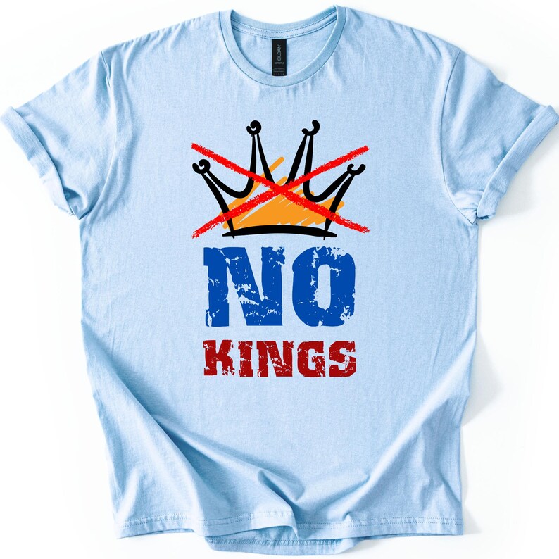 May include: Light blue t-shirt with a graphic design. The design features a black and orange crown crossed out with a red line, and the words "NO KINGS" in blue and red distressed font.