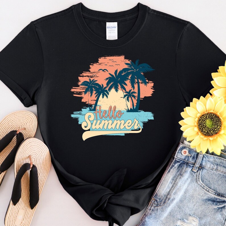 K&ouml;nnte beinhalten: Schwarzes T-Shirt mit einem farbenfrohen Aufdruck von Palmen, einem Sonnenuntergang und dem Text "Hello Summer". Das Design verwendet Orange-, Blau- und Gelbt&ouml;ne. Das Shirt wird mit Jeansshorts und Sandalen gezeigt.