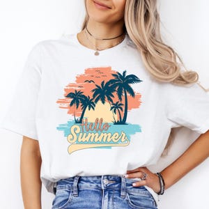 K&ouml;nnte beinhalten: Wei&szlig;es T-Shirt mit tropischem Design. Das Design zeigt Palmen, einen Sonnenuntergang und die Worte "Hello Summer" in einem Retro-Schriftzug. Das Design umfasst Blau-, Orange- und Gelbt&ouml;ne und erinnert an ein Strandurlaubsthema.