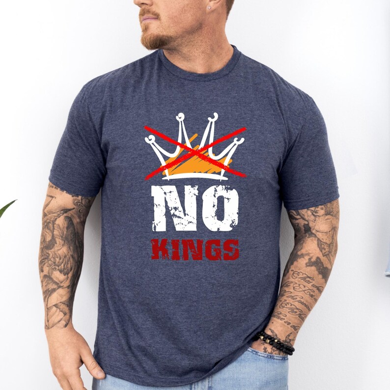 May include: Navy blue t-shirt with a graphic design. The design features a crossed-out crown above the word "NO" in white, and the word "KINGS" in red. The shirt is short-sleeved.