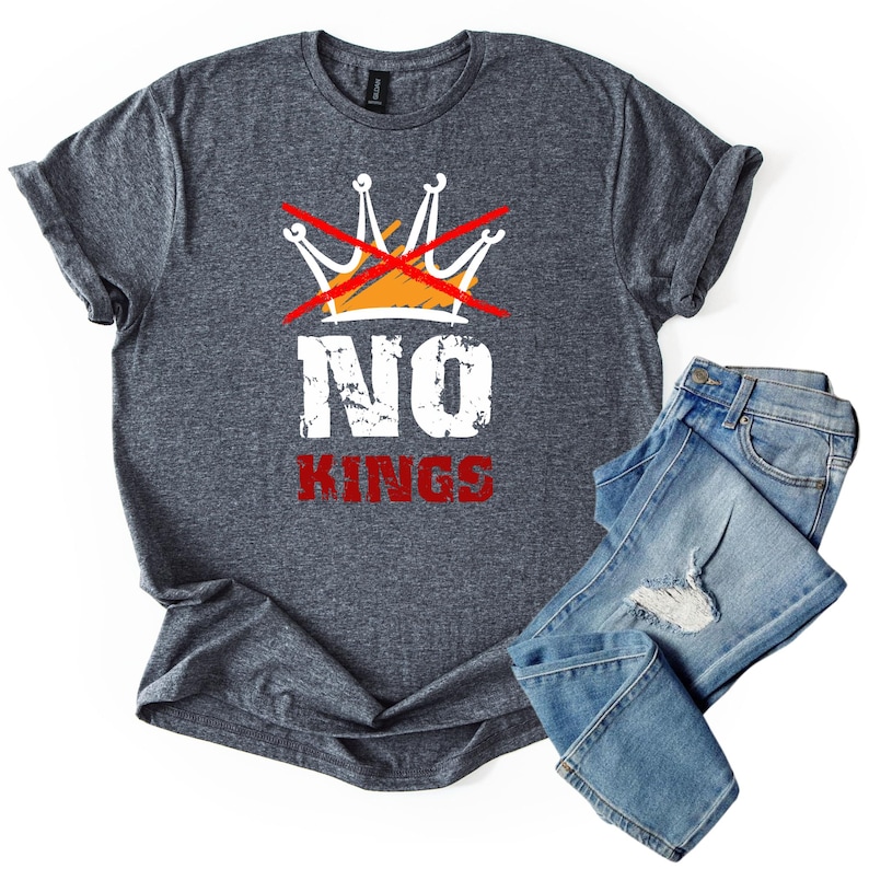 May include: A heather gray t-shirt with the words "NO KINGS" in white and red, with a crossed-out crown graphic. The shirt is paired with a pair of blue jeans.