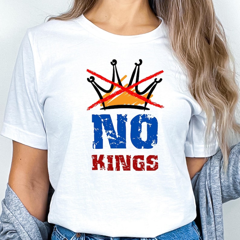 May include: White t-shirt with a graphic design. The design features a black crown crossed out with a red line, above the words "NO KINGS" in blue and red distressed font.