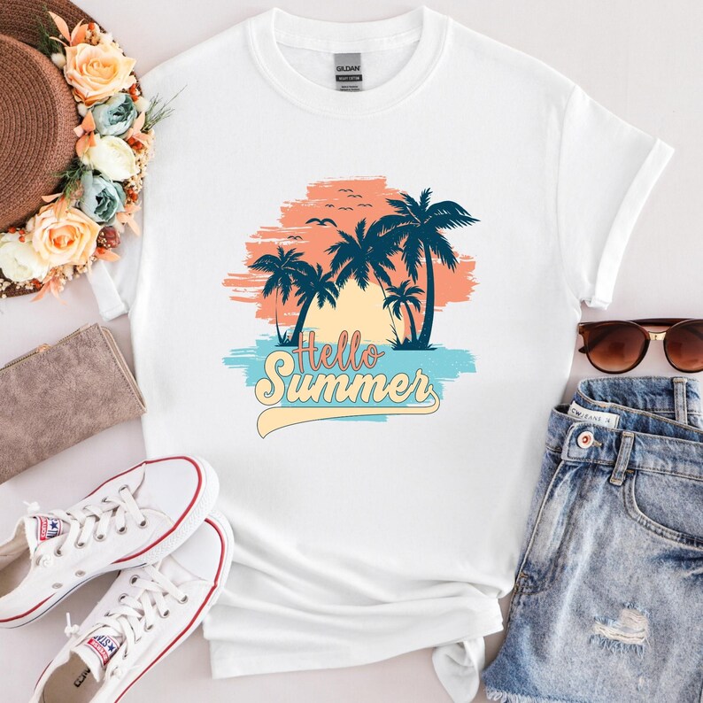 K&ouml;nnte beinhalten: Wei&szlig;es T-Shirt mit tropischem Design. Das Design zeigt Palmen, einen Sonnenuntergang und den Text "Hello Summer" in einem Retro-Schriftzug. Das Design enth&auml;lt Blau-, Orange- und Gelbt&ouml;ne und erinnert an ein Strandurlaubsthema.