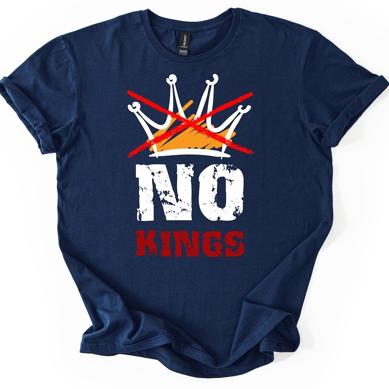 May include: Navy blue t-shirt with a graphic design. The design features a crown crossed out with a red line, the word "NO" in white, and the word "KINGS" in red. The shirt is folded.