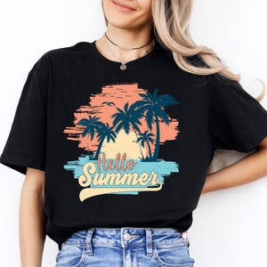 K&ouml;nnte beinhalten: Schwarzes T-Shirt mit einem farbenfrohen Grafikdesign. Das Design zeigt Palmen, einen Sonnenuntergang und die Worte "Hello Summer" in einer stilisierten Schriftart. Das Shirt ist ein l&auml;ssiger, bequemer Stil.