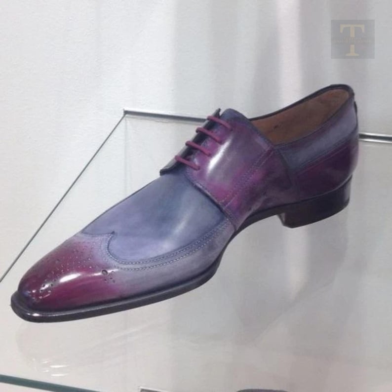 May include: A single, two-tone leather dress shoe. The shoe transitions from a deep burgundy at the toe to a light blue-grey at the midfoot. The shoe has a wingtip design with burgundy laces and a black sole.