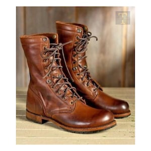 Puede incluir: Un par de botas de combate de cuero marrón con un diseño de cordones. Las botas tienen un aspecto desgastado y envejecido, con costuras visibles y ojales metálicos. Las suelas son de un marrón más oscuro y las botas parecen nuevas.