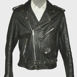 May include: A black leather biker jacket with an off-centre zip fastening. It has multiple zipped pockets, a belted waist, and press-stud lapels. The jacket is displayed on a mannequin, revealing a white collared shirt underneath.