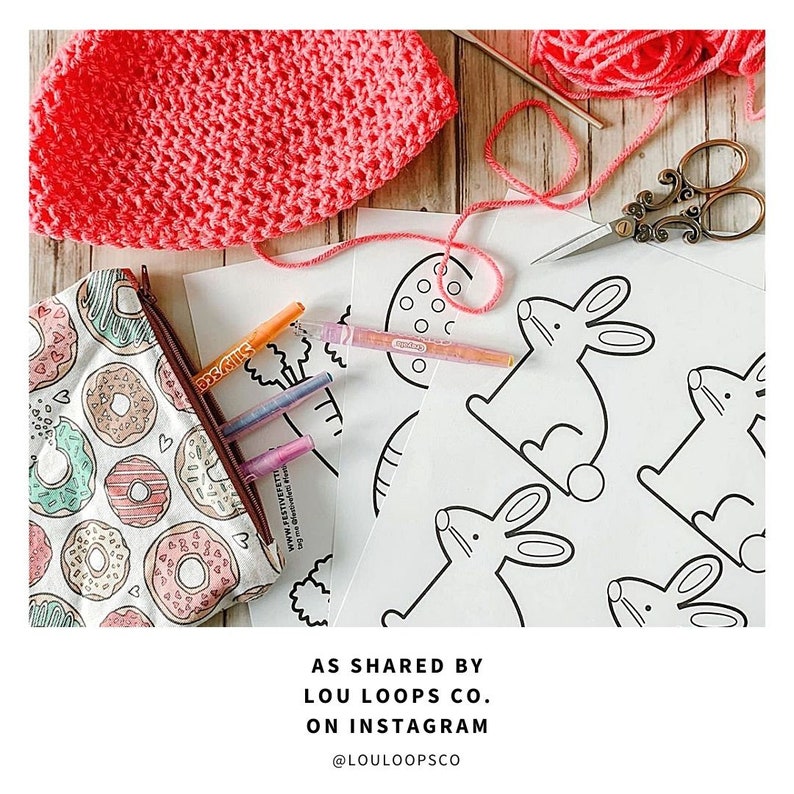 May include: A set of printable coloring pages featuring bunny rabbits, an egg, and a tree. The pages are on white paper and are ready to be colored. The image also includes a pink crocheted hat, a pencil case with a donut pattern, and a pair of scissors.