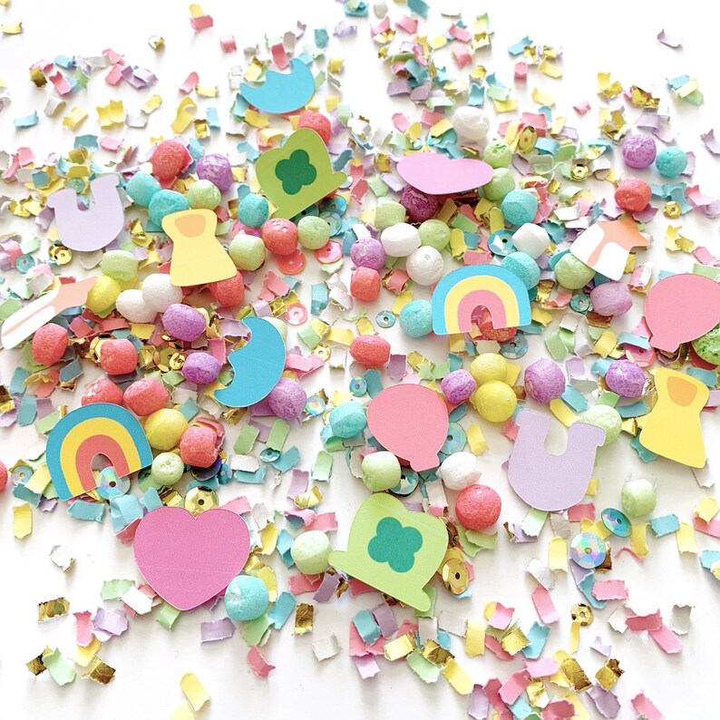 May include: A colorful assortment of confetti, small foam balls, and paper cutouts. The cutouts include rainbows, hearts, shamrocks, and crescent moons. The confetti is in shades of pink, yellow, green, and gold. The foam balls are in various pastel colors.