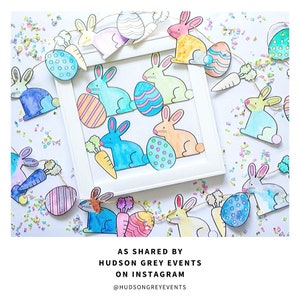 May include: A colorful Easter bunny garland with watercolor painted bunnies and eggs. The garland is strung with twine and has a carrot hanging from each bunny. The garland is displayed on a white surface with confetti.