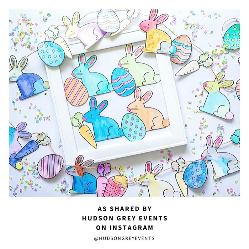 May include: A colorful Easter bunny garland with watercolor painted bunnies and eggs. The garland is strung with twine and has a carrot hanging from each bunny. The garland is displayed on a white surface with confetti.