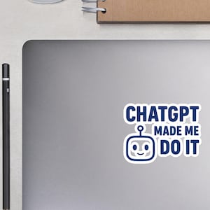 May include: A laptop with a sticker saying "ChatGPT MADE ME DO IT" in navy blue text and a robot graphic. A white mouse, a spiral-bound notebook, a pencil, glasses, and small potted plants are also visible.