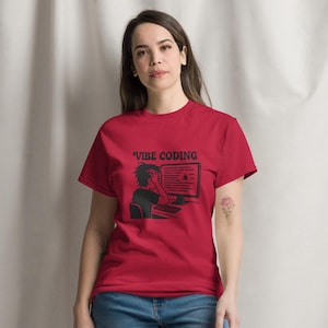 Puede incluir: Una camiseta roja con el texto "Vibe Coding" y un gráfico negro de una persona codificando en una computadora. La persona lleva vaqueros azules y zapatillas blancas.