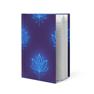 May include: A hardback notebook with a dark purple cover featuring a repeating pattern of glowing blue lotus flower designs. The notebook is open, revealing lined white pages. The design is modern and eye-catching.