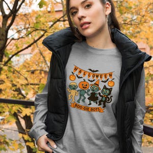 May include: A grey long-sleeve shirt featuring a graphic print of cartoon robots and a cat dressed for Halloween. The design includes orange pumpkins, bats, and a banner with the text HALLOWEEN and BOO-GIE BOTS in orange and black colors.