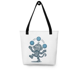 May include: White tote bag with a cartoon monkey juggling binary code. The monkey is grey, and the binary code balls are light blue. The bag has black handles and a black top.
