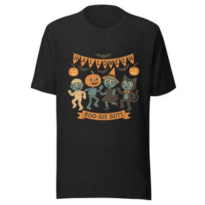 May include: Dark gray t-shirt featuring a Halloween-themed graphic. The design includes a banner that reads "HALLOWEEN" above cartoon characters dressed as a mummy, pumpkin, witch, and cat. The text "BOO-GIE BOTS" is below the characters.