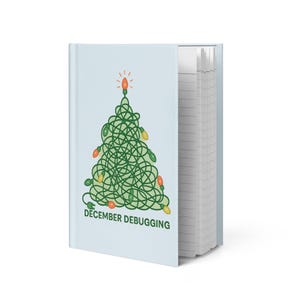 May include: A light blue notebook with a Christmas tree design made of green lines and colorful lights. The text "DECEMBER DEBUGGING" is printed below the tree. The notebook is open, revealing lined pages.