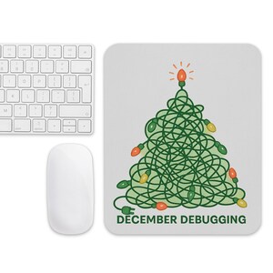 May include: A white computer mouse and keyboard are next to a rectangular mousepad. The mousepad features a green Christmas tree design made of tangled lights, with the text "DECEMBER DEBUGGING" at the bottom.