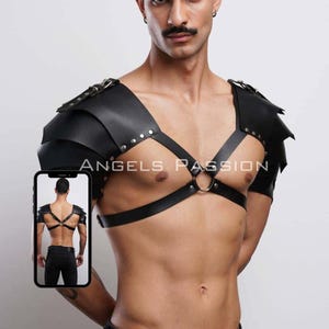 Può includere: Armatura per spalle in pelle nera con rivetti e cinghie argentate, con un design a pettorina. L'immagine include un inserto più piccolo che mostra la vista posteriore dell'armatura. Il testo "ANGELS PASSION" è visibile.