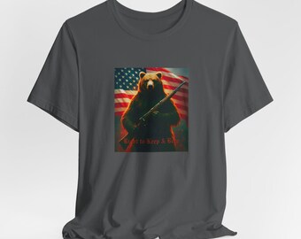 Puede incluir: Camiseta gris oscuro con un gráfico de un oso sosteniendo un rifle frente a una bandera estadounidense. El texto "Right to Keep & Bear" está impreso debajo del oso. La camiseta está hecha de un material suave.