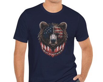 Puede incluir: Camiseta azul marino con un diseño de cabeza de oso que incorpora la bandera estadounidense. El texto "RIGHT TO KEEP & BEAR" está impreso en un emblema en forma de escudo debajo de la cabeza del oso.