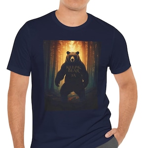 May include: Navy blue t-shirt with a bear graphic set in a forest. The bear has the text "KEEPS & BEAR 2A" on its chest. The background depicts a forest with sunlight streaming through the trees.