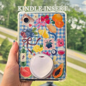 Könnte beinhalten: Transparenter Kindle-Einsatz mit blau-weißem Karomuster, verziert mit Früchten, einer Weinflasche, einer rosa Kamera und anderen sommerlichen Bildern. Der Einsatz hat einen weißen herzförmigen Griff.