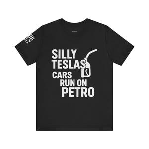 May include: Black t-shirt with white text and a gas pump graphic. The text reads "SILLY TESLAS CARS RUN ON PETRO." The shirt also has a small American flag graphic on the left sleeve.