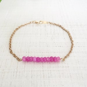 Könnte beinhalten: Ein zartes Armband aus einer goldenen Kette mit einer Reihe von rosafarbenen Edelsteinperlen.