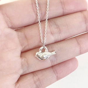 May include: A silver necklace with a heart-shaped pendant featuring a small bird resting inside. The bird is facing to the right.