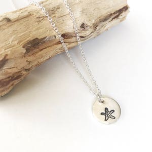 May include: A silver necklace with a small, round pendant featuring a simple, hand-drawn starfish design.